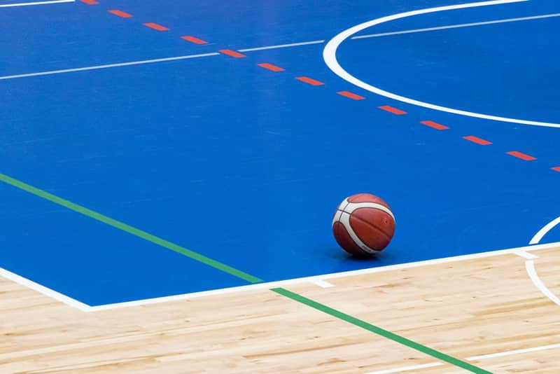 A basketball resting on the wooden edge of an indoor court